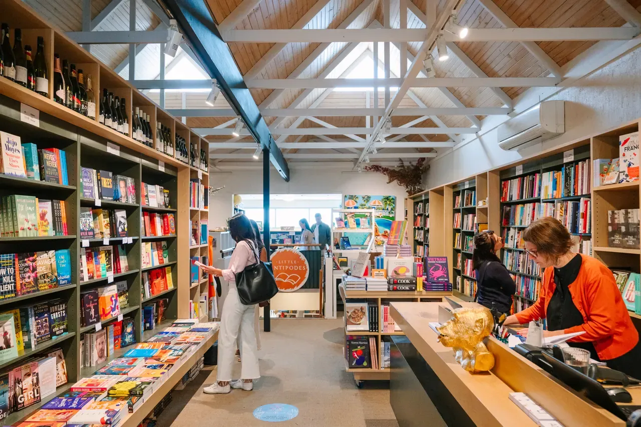 Inside Antipodes Bookshop in Sorrento, with book-lined walls, a pitched timber ceiling and a staff member at the front counter