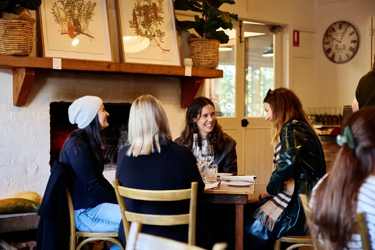 A group of friends talk over wine at a table near the fireplace and botanical prints at Merricks General Wine Store