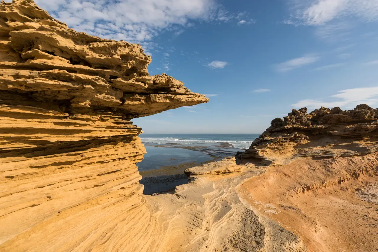 Layered sandstone ledges frame a view of a rock pool and surf on the ocean coast at Portsea