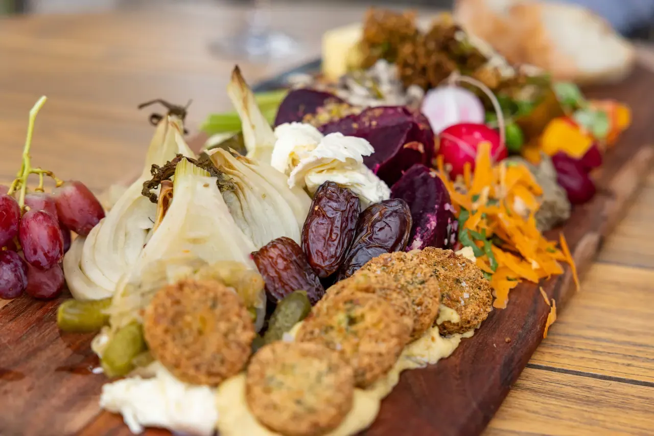 A grazing board of roasted fennel, beetroot, dates, grapes, fritters and grated carrot on a timber table