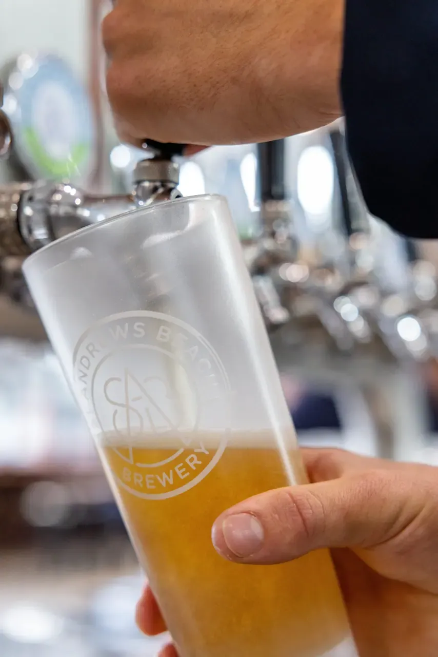 Close view of a hand pulling a tap to fill a St Andrews Beach Brewery glass with pale beer