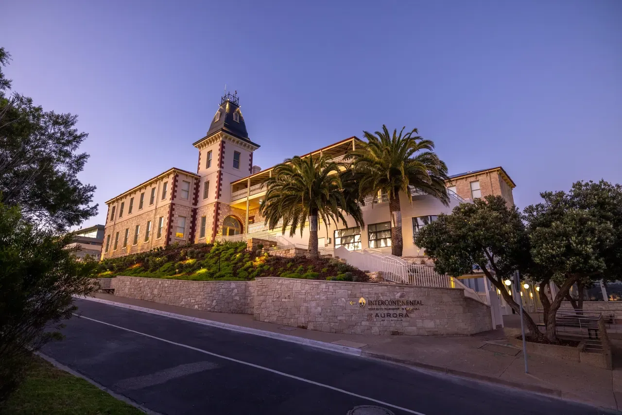 The Continental Sorrento at dusk, its limestone tower and palm trees rising above a stone retaining wall along a curving road