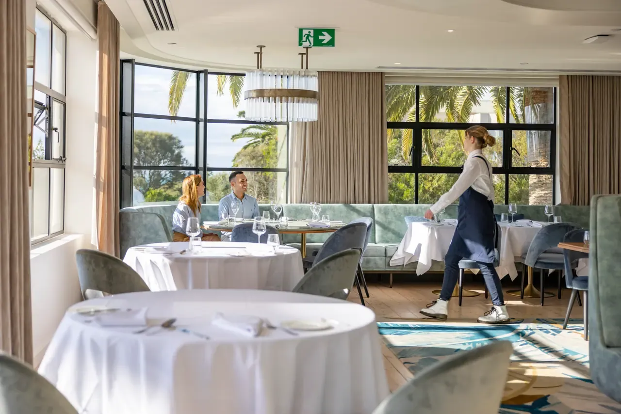 Dining room at Audrey's, The Continental Sorrento, with white-clothed tables, velvet chairs and windows onto palms and garden