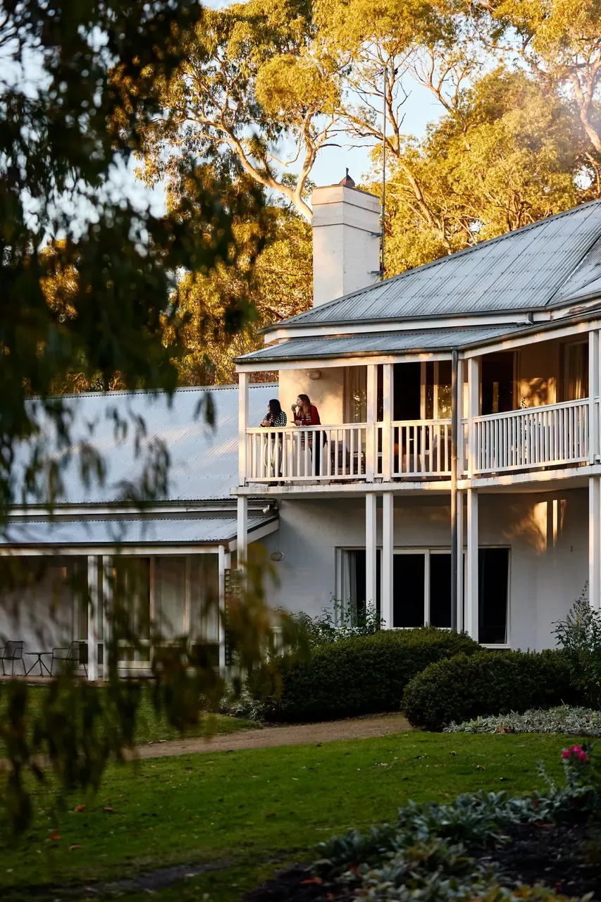 White two-storey homestead at Lindenderry at Red Hill in late light, two guests on the upstairs verandah above a garden lawn