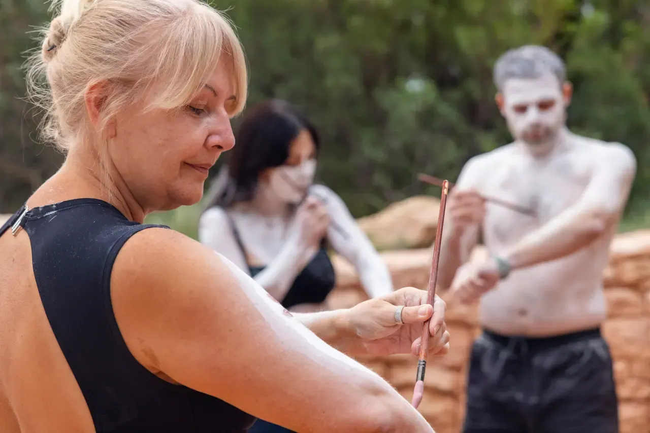 Guests take part in a body-painting session with white ochre and fine brushes beside a stone wall at Peninsula Hot Springs