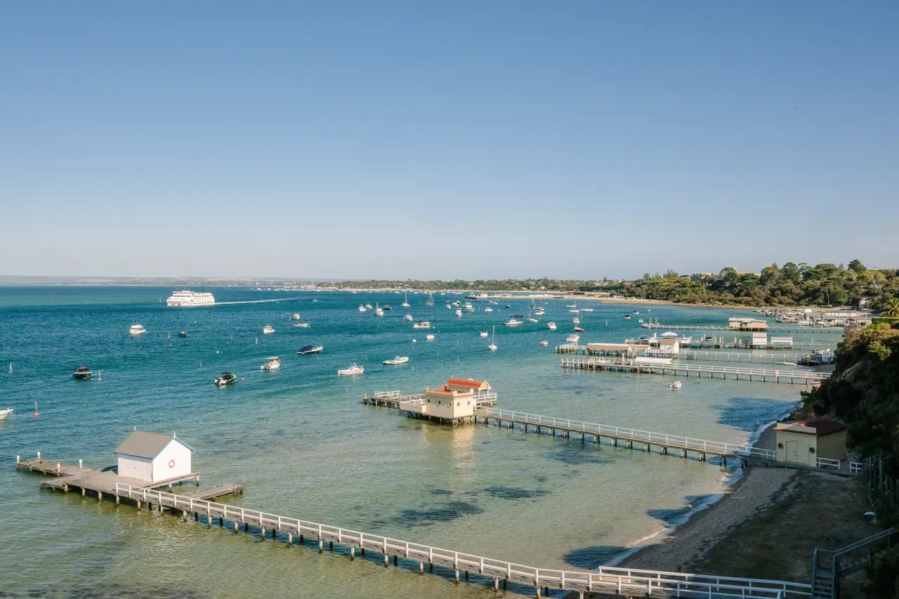 View from Millionaire's Walk over long private jetties, boat sheds and moored boats, with a ferry crossing the bay