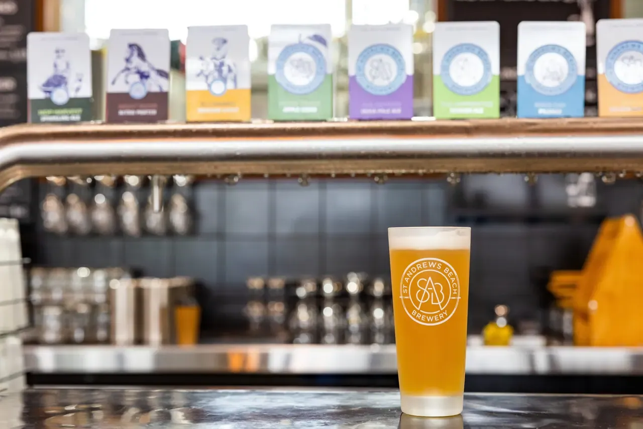 A pint of pale beer in a branded glass on the bar at St Andrews Beach Brewery, with beer tap badges lined up above