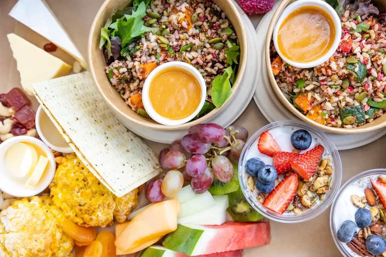 Overhead view of a shared platter with grain salads, cheese, crispbread, fresh fruit and berry yoghurt cups at Peninsula Hot Springs