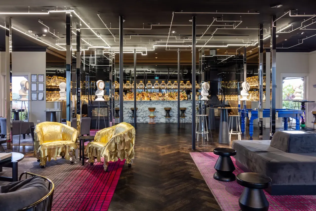 Lounge bar at Jackalope Hotel with gold chairs, pink rugs, a blue pool table, sculpted busts and a marble bar under linear lights