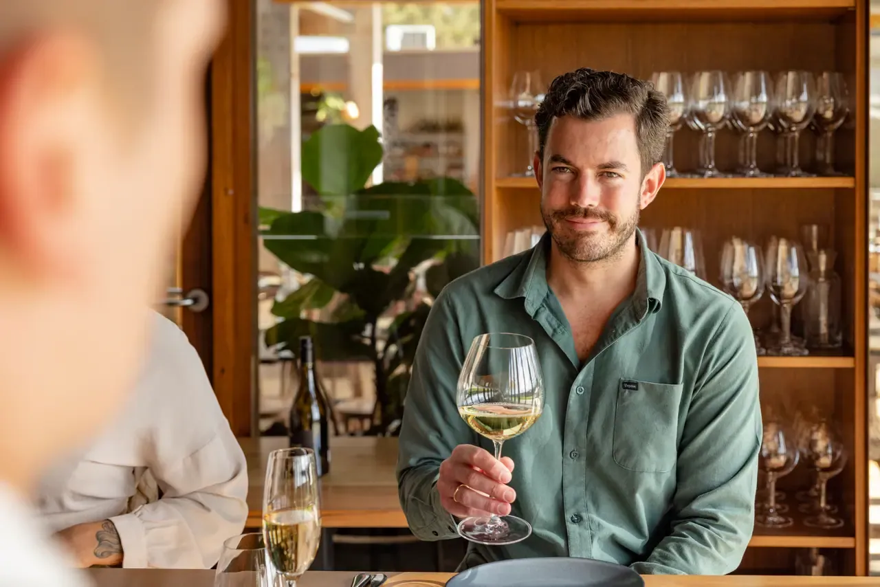 A diner raises a glass of white wine at a table in front of shelves of stemware inside the Montalto restaurant