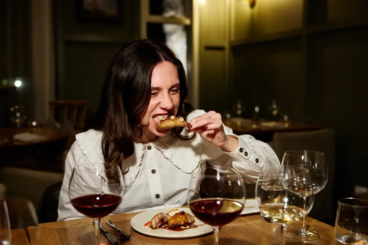 A diner bites into a roasted dish at a candlelit restaurant table set with glasses of red and white wine