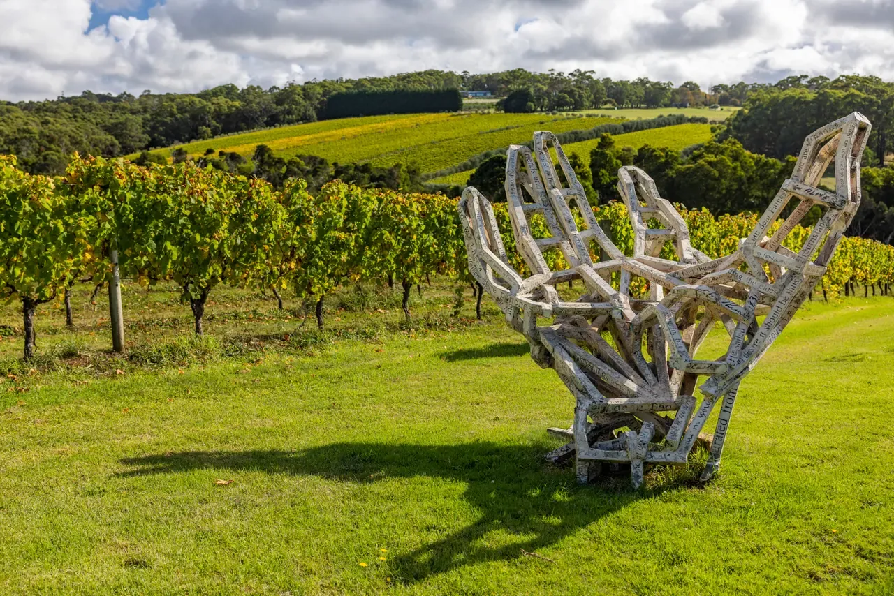 Large open lattice sculpture on a grassy slope beside autumn-tinged vines at Montalto, with rolling vineyards beyond