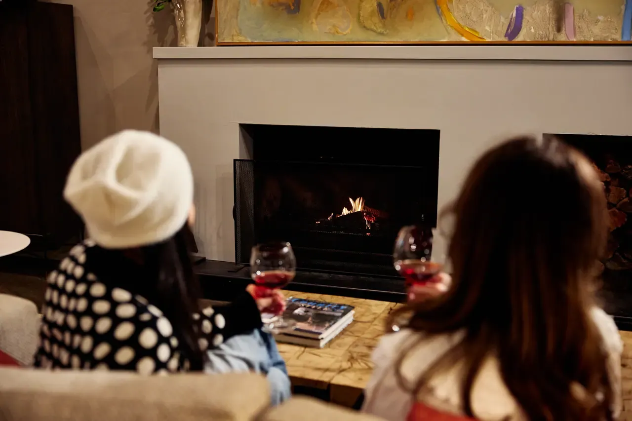 Two guests with glasses of red wine sit before an open fireplace in a lounge at Lindenderry at Red Hill