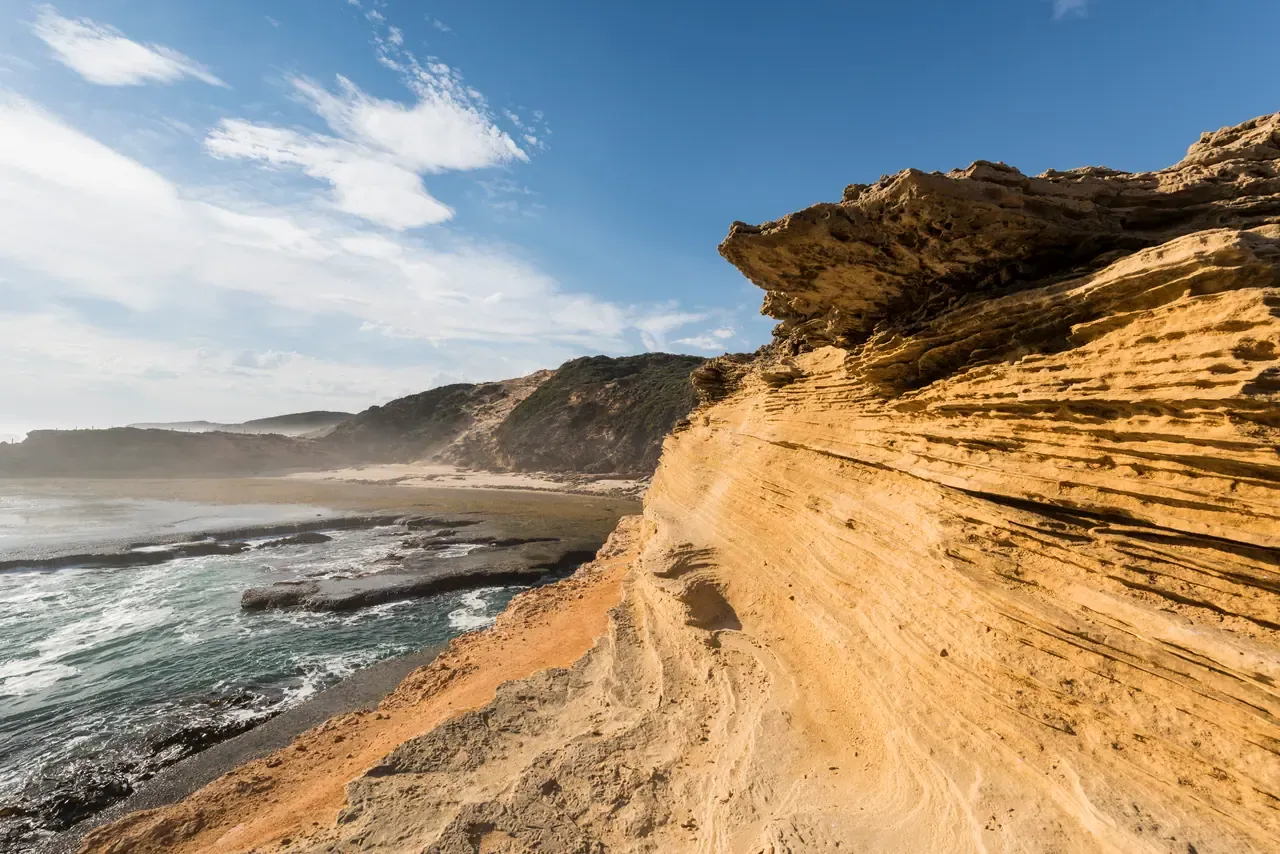 Wind-carved golden sandstone cliffs above a rock platform and surf on the ocean coast at Portsea