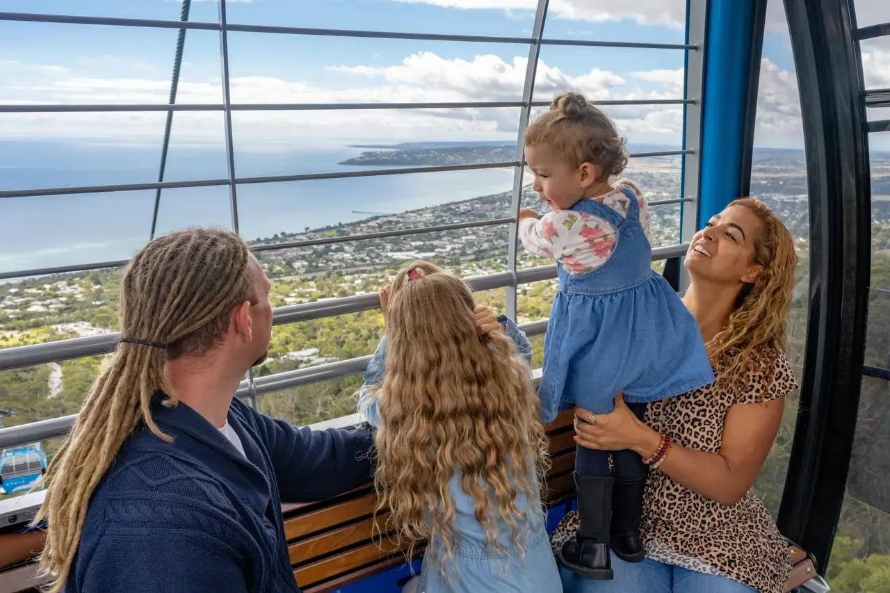A family looks out from inside an Arthurs Seat Eagle gondola over the bayside suburbs and Port Phillip below
