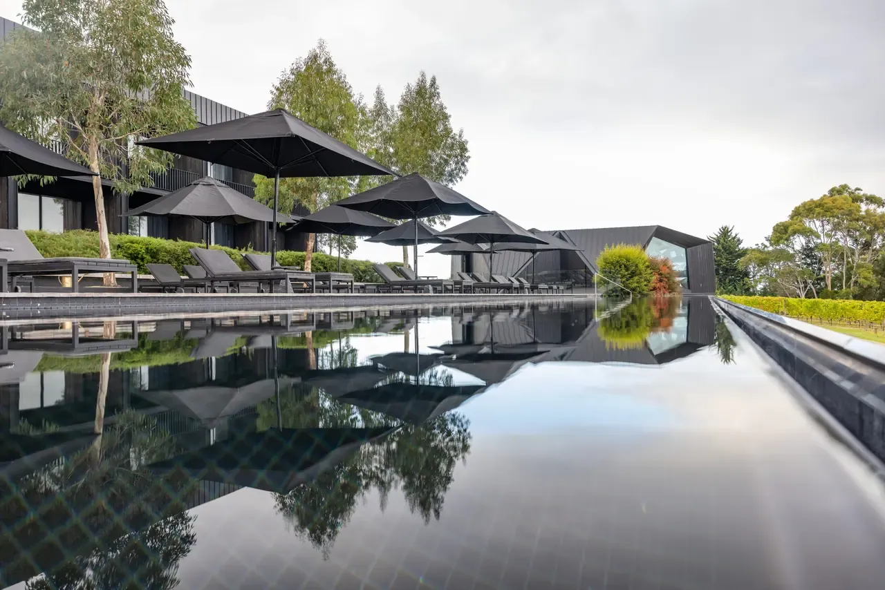 Black infinity pool at Jackalope Hotel reflecting black umbrellas, sun loungers, gum trees and the dark angular hotel buildings