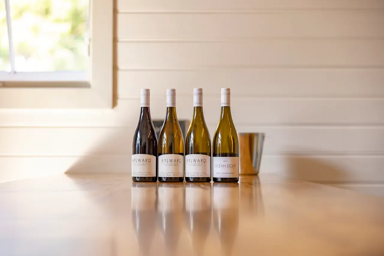 Four bottles of white and red wine, including an Ocean Eight chardonnay, stand in a row on a polished bench