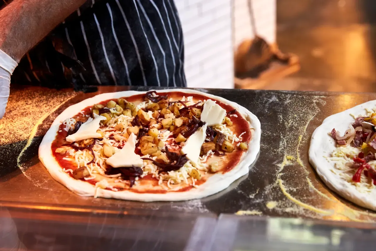 An uncooked pizza topped with potato, caramelised onion and cheese on a floured bench, ready for the oven