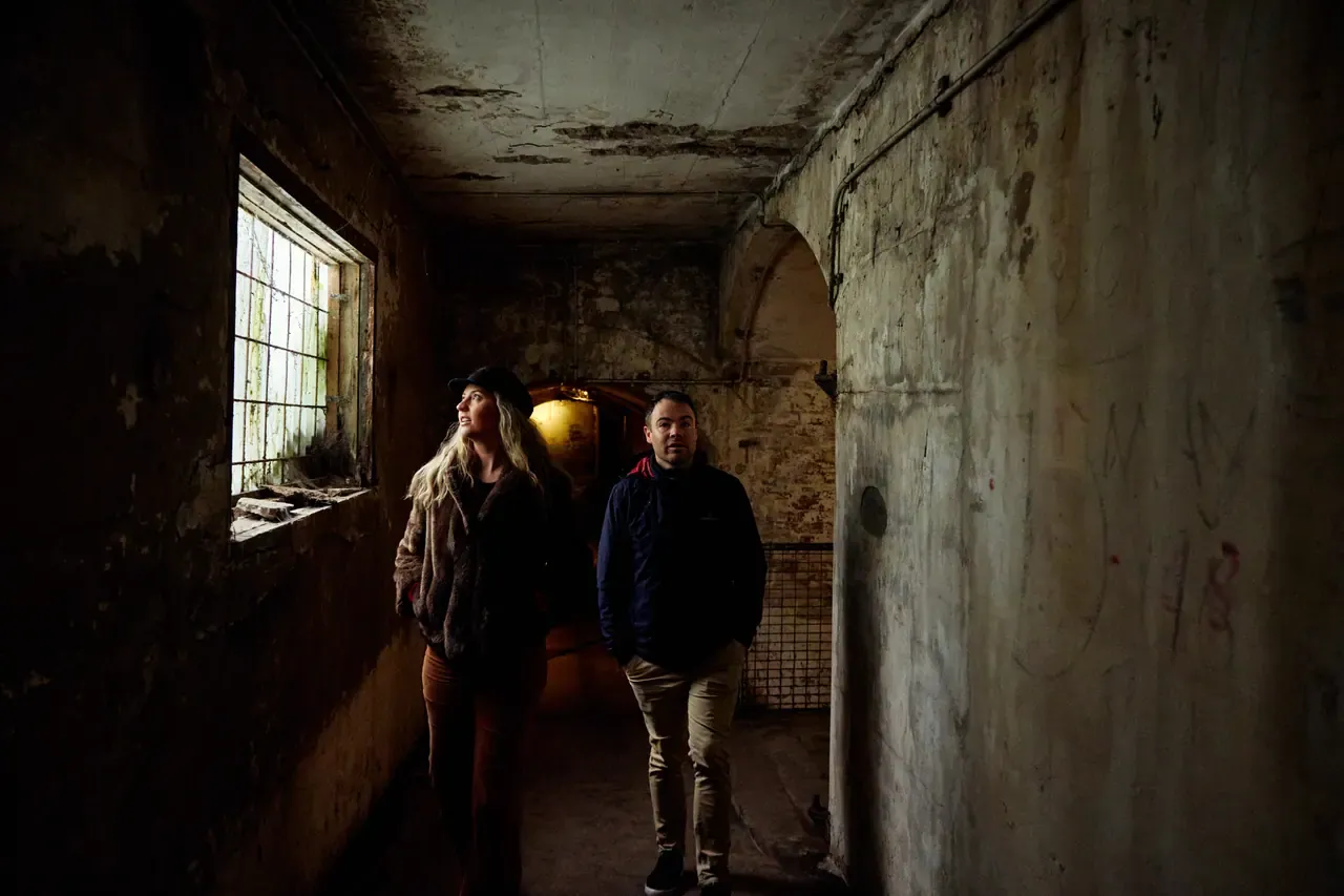 Two visitors walk through a dim, weathered concrete corridor inside the old fortifications at Point Nepean National Park