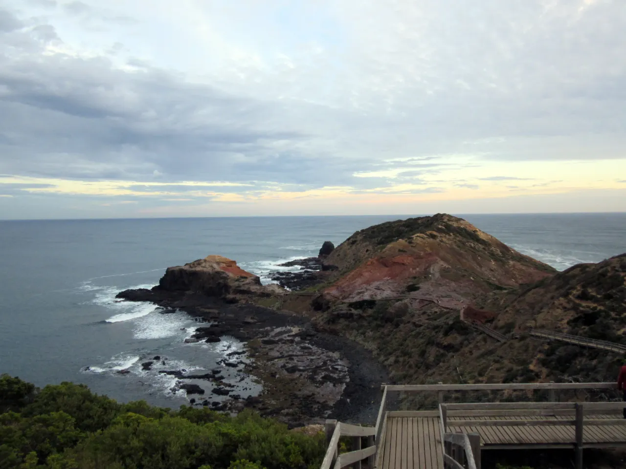 A timber boardwalk above the rocky Cape Schanck shore, with a sea stack offshore.