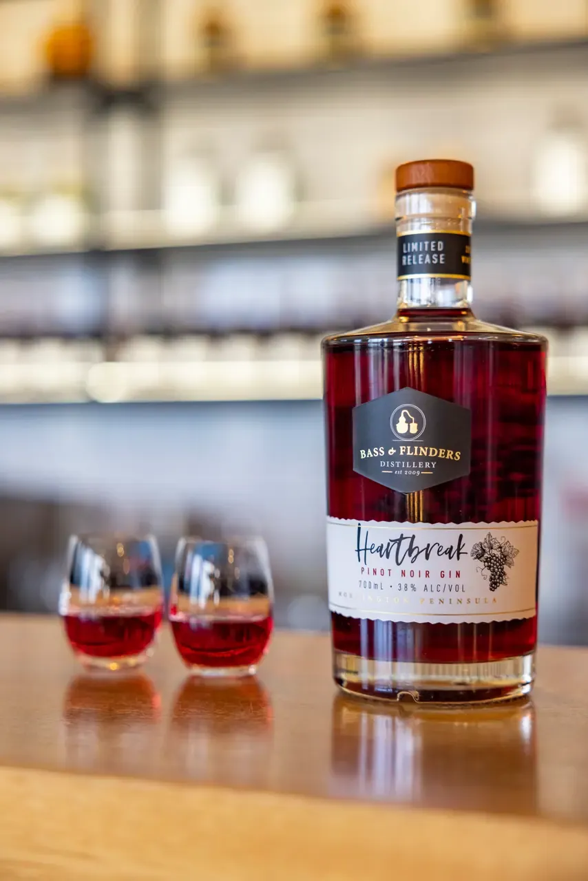 A bottle of Bass and Flinders Heartbreak pinot noir gin on the bar beside two small glasses of the ruby spirit