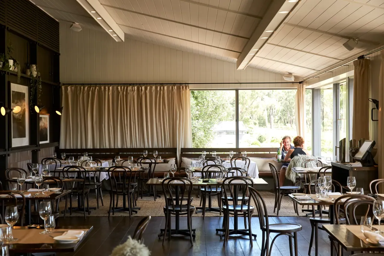 Dining room at Polperro Winery with bentwood chairs, set tables, a pitched white ceiling and large windows onto the garden