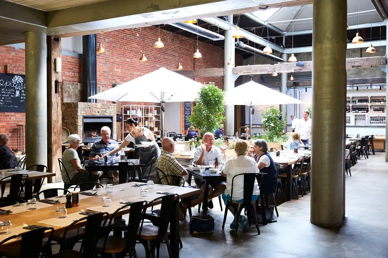 Diners at communal tables under white umbrellas in the brick-walled, warehouse-style hall at The Epicurean, Red Hill