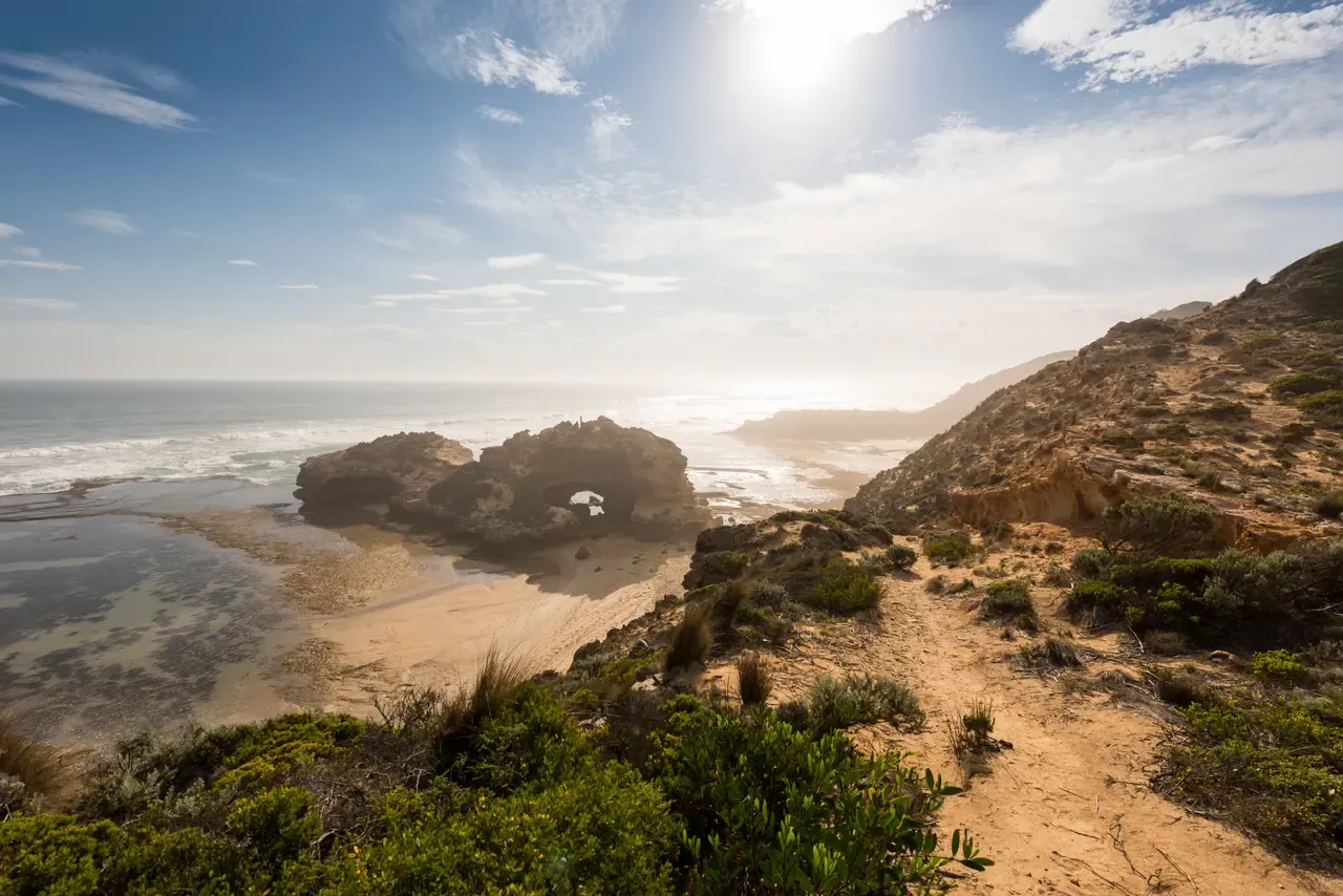 The London Bridge rock arch standing in the shallows below a sandy clifftop track on the ocean coast near Portsea