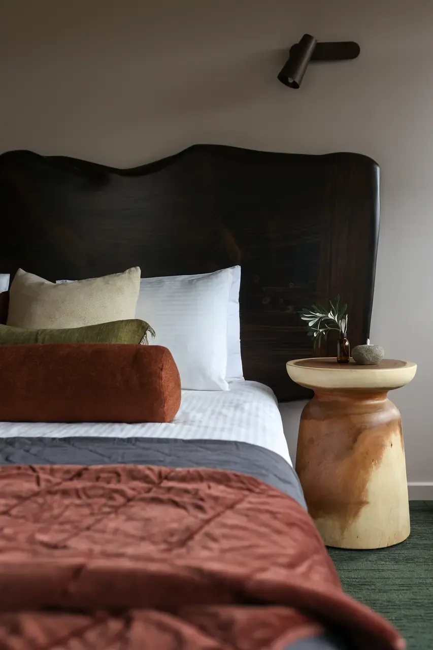 Bed with a live-edge timber headboard, rust velvet quilt and turned timber side table in a Peninsula Hot Springs Eco Lodge
