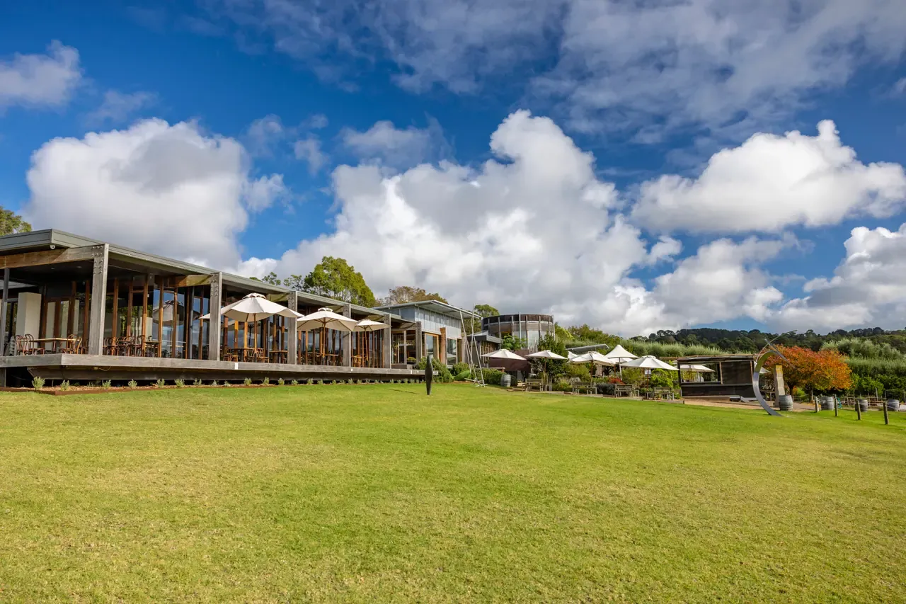 The restaurant at Montalto with white umbrellas along its deck, set above a broad sloping lawn under a blue sky with cloud