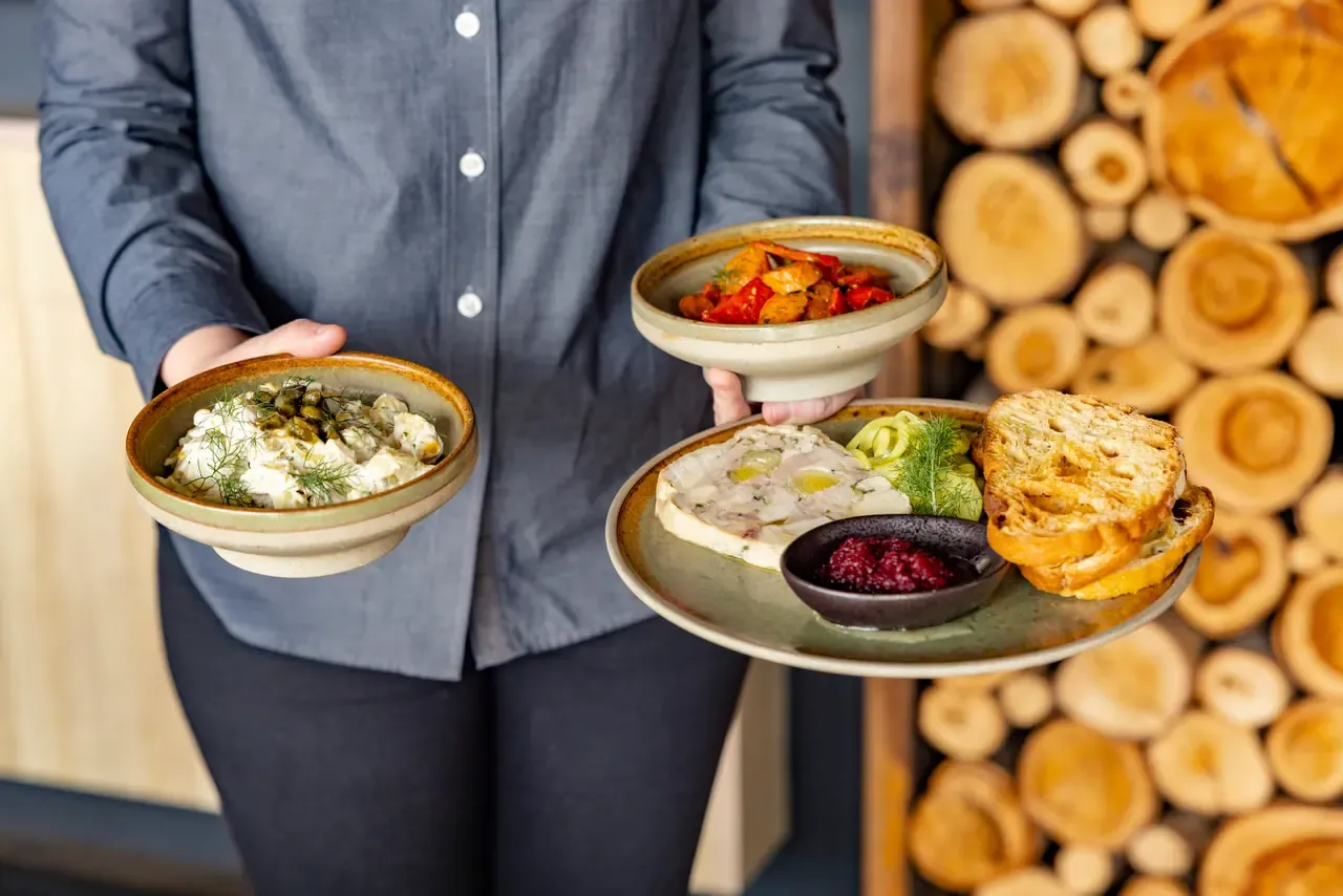 A server holds bowls of potato salad and roasted capsicum and a plate of terrine with toast and beetroot at Montalto