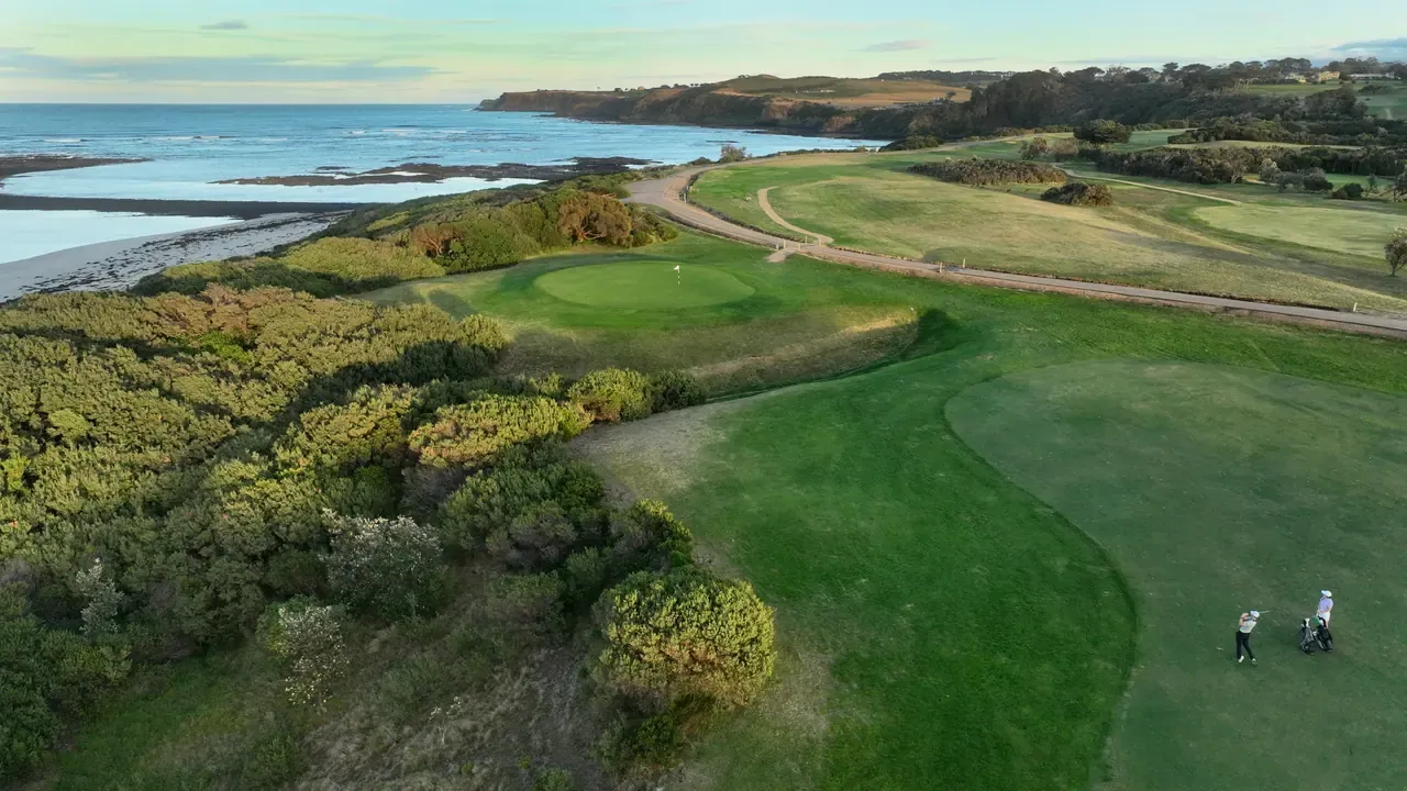 Aerial view of Flinders Golf Course with a golfer playing from a fairway, greens beside scrub and the ocean in the distance.