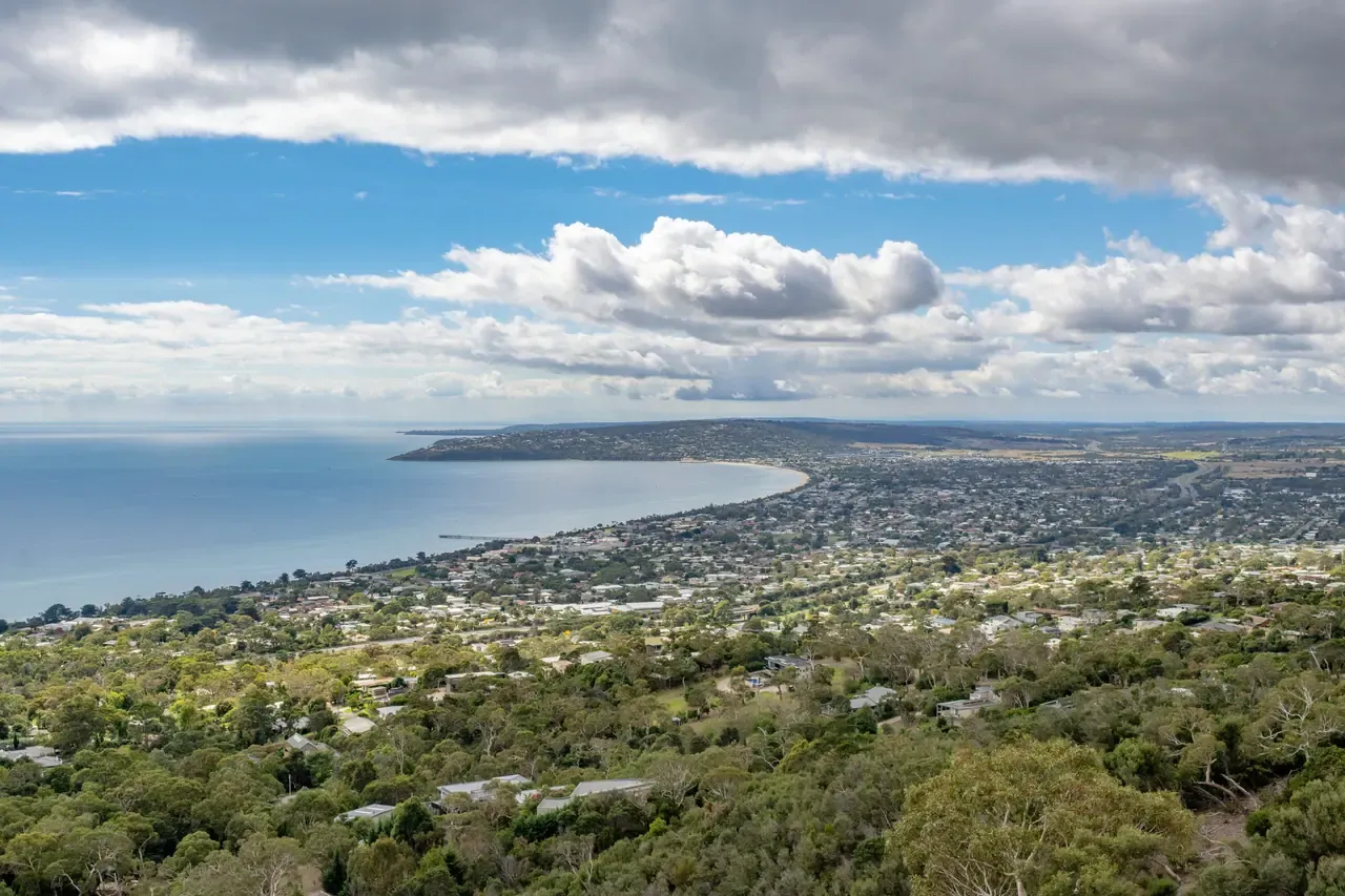 View from Arthurs Seat over bushland and bayside suburbs curving around Port Phillip Bay under broken cloud