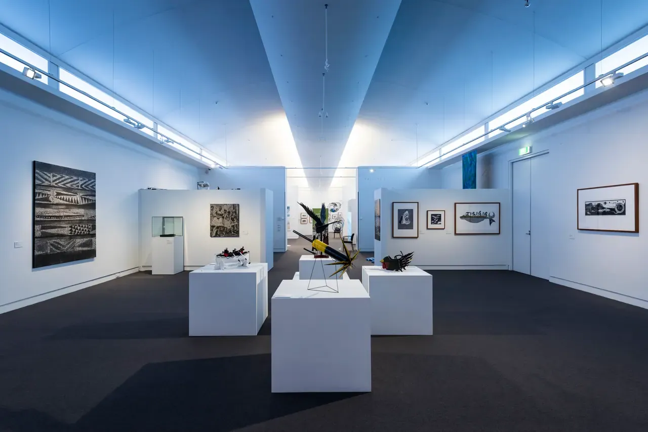 Gallery room at Mornington Peninsula Regional Gallery with framed prints on white walls and sculptures on plinths under a vaulted ceiling