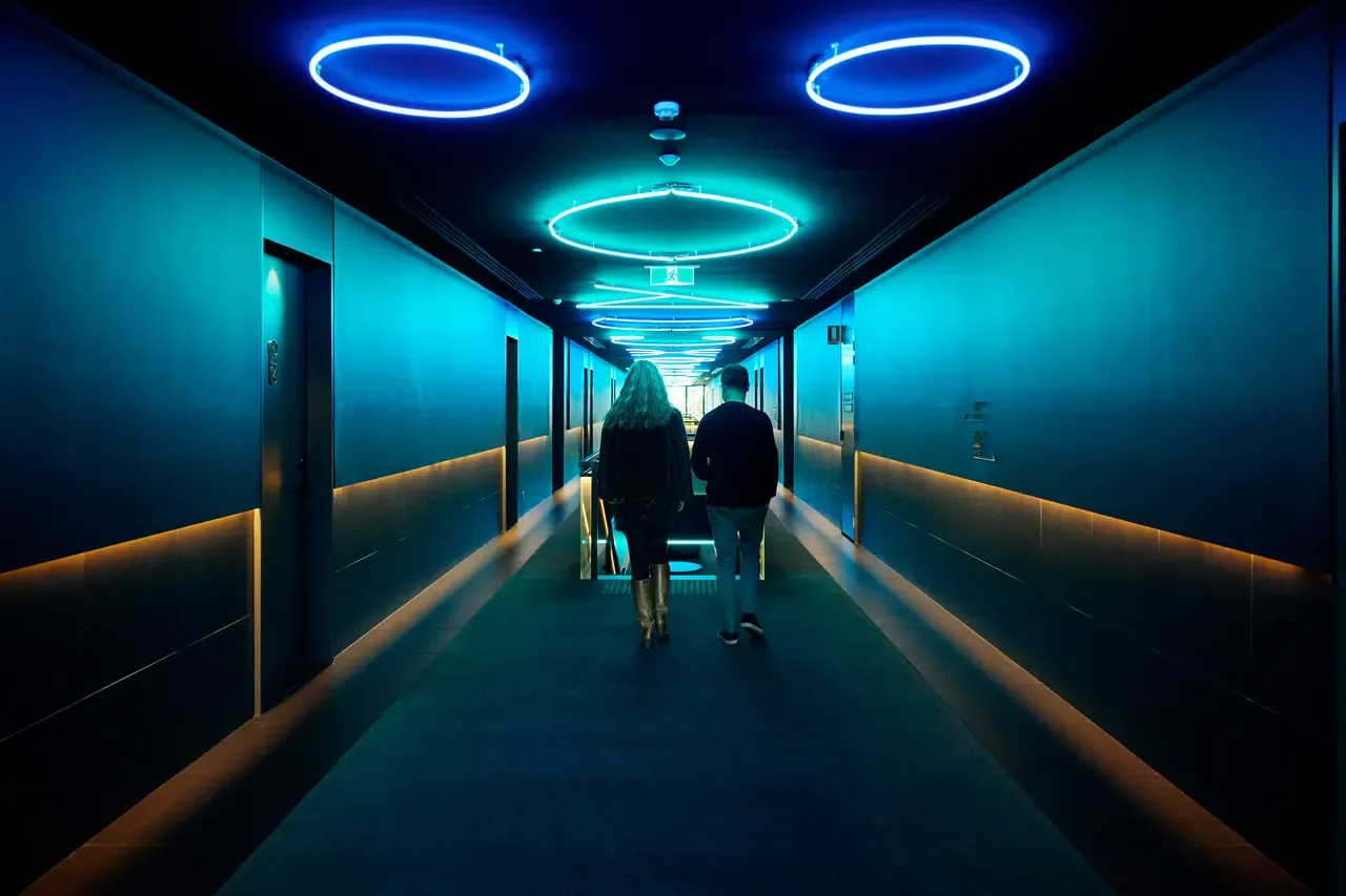Two guests walk down a dark corridor lit by blue neon ring lights and low amber strips at Jackalope Hotel