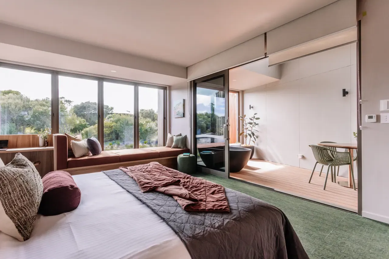 Eco Lodge bedroom at Peninsula Hot Springs with a made bed, bush-view window seat and a deck holding an outdoor bath