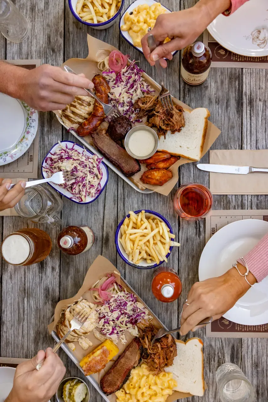 Overhead view of diners sharing trays of brisket, sausage, pulled pork, coleslaw, chips and mac and cheese