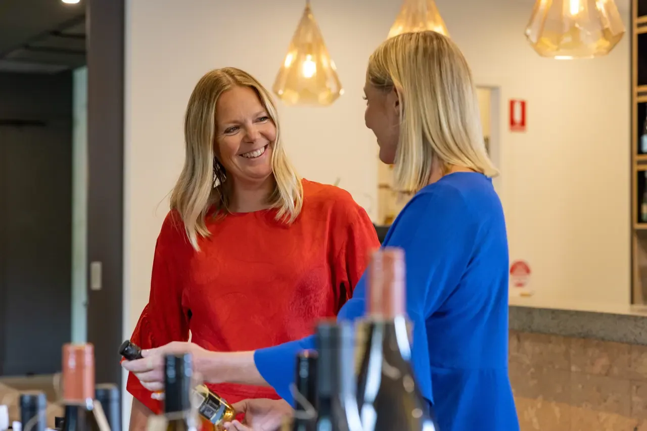 A staff member in red shows a bottle of wine to a visitor across the tasting bench at the Crittenden Estate cellar door