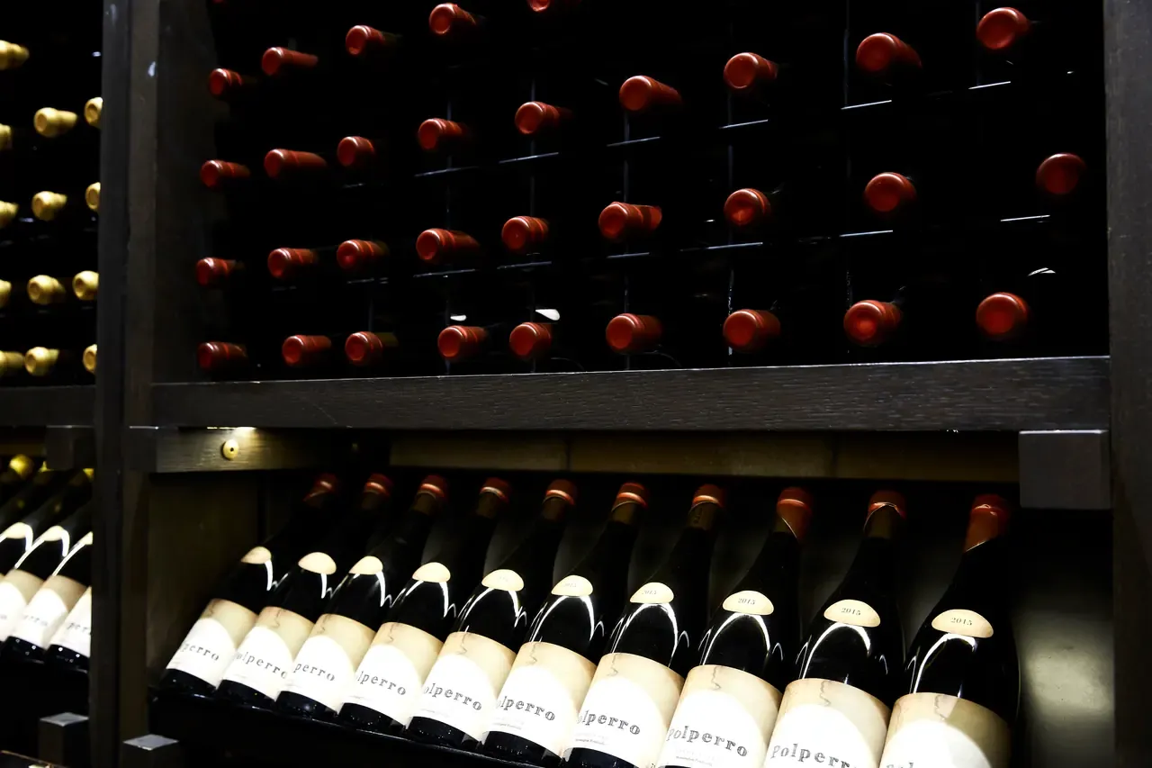 Rows of wine bottles stored in dark timber racks in the cellar at Polperro Winery, with labelled bottles on the lower shelf