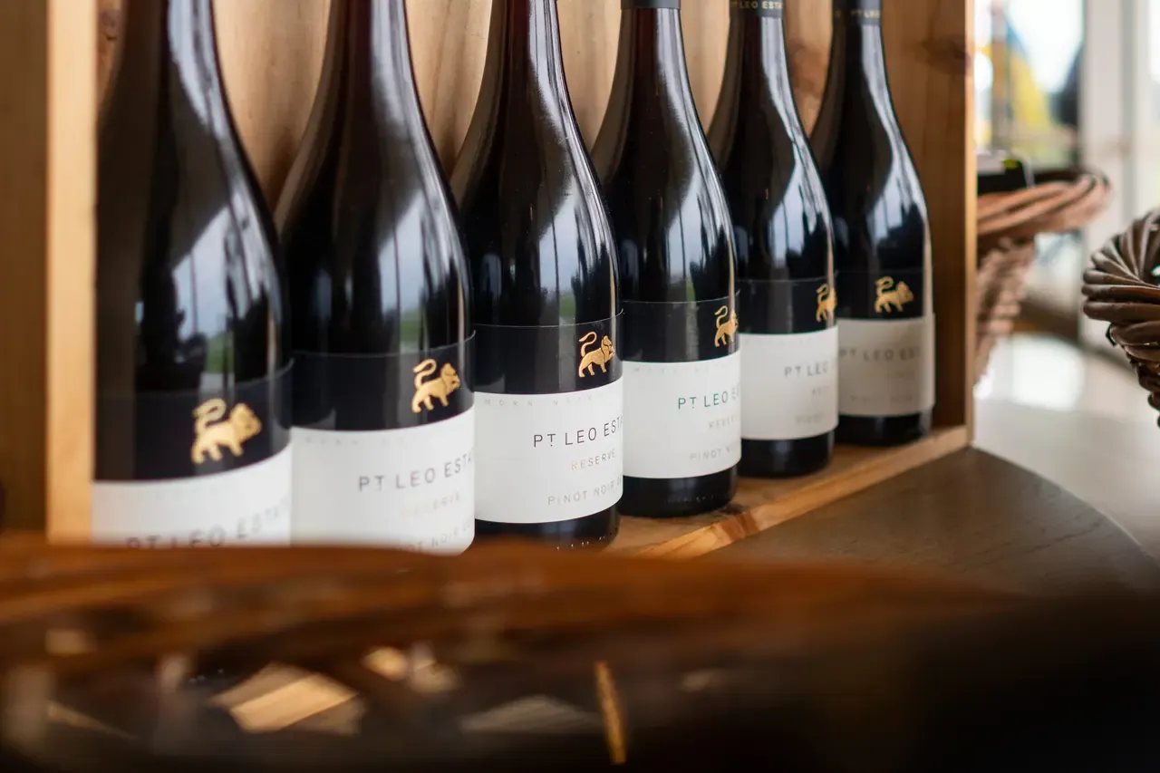 Row of Pt. Leo Estate Reserve Pinot Noir bottles with gold lion emblems lined up on a timber shelf