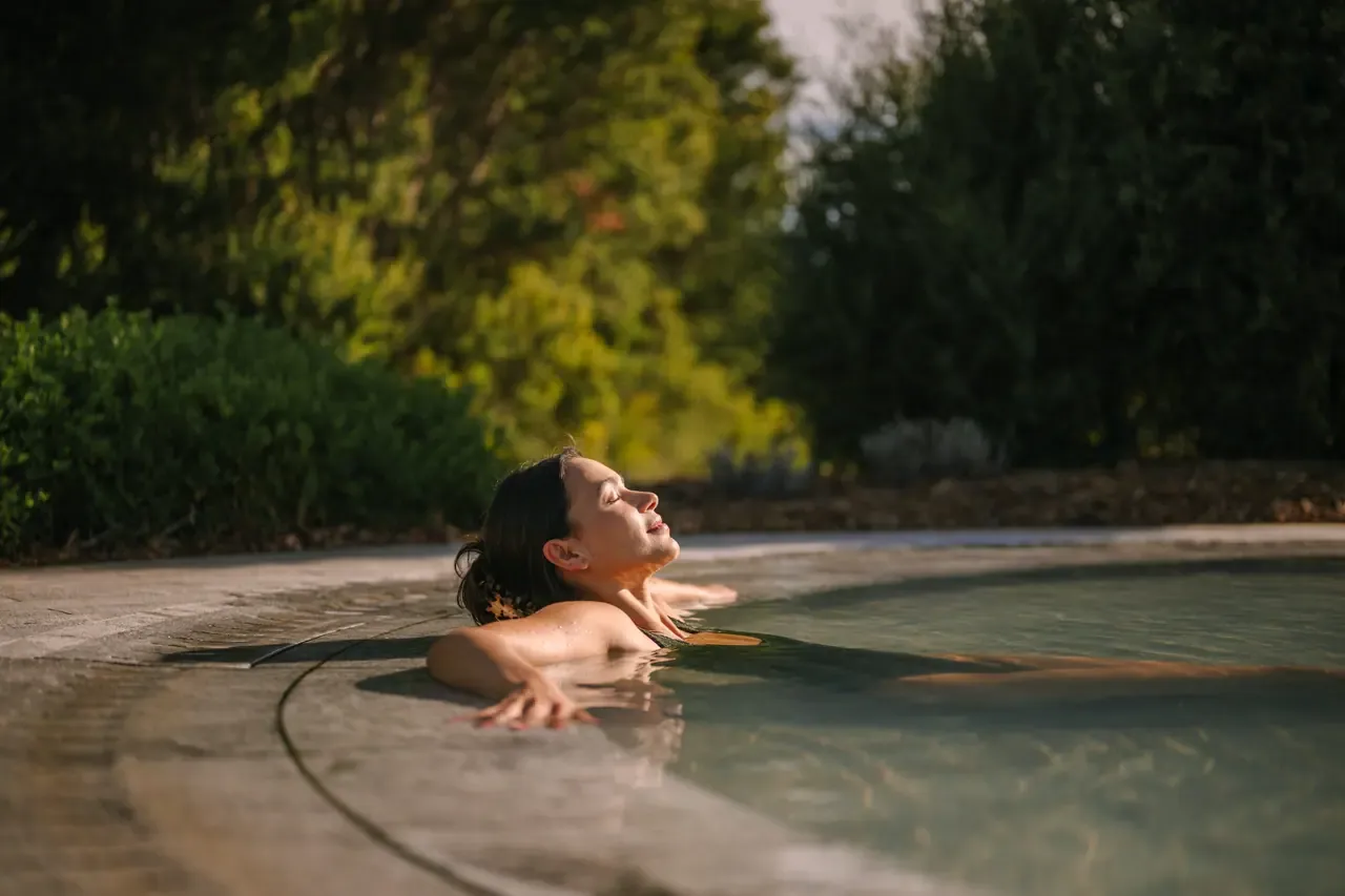A bather leaning back with eyes closed at the edge of a warm pool in late sun at Alba Thermal Springs