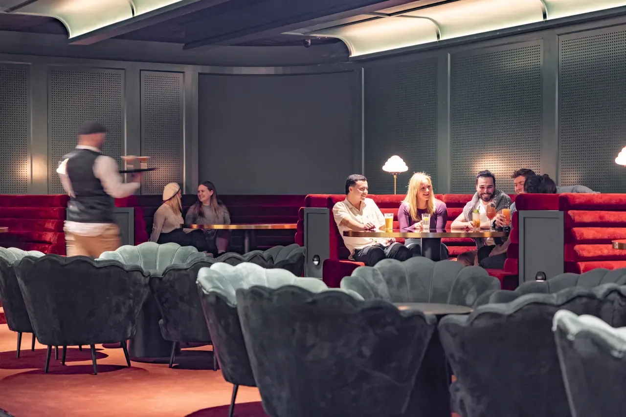Guests share drinks in red velvet booths at Barlow, The Continental Sorrento, as a waiter carries a tray past scalloped armchairs