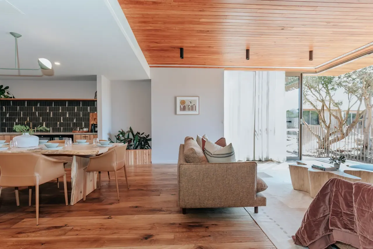 Open-plan Eco Lodge living area at Peninsula Hot Springs with timber ceiling, dining table, sofa and doors open to a courtyard