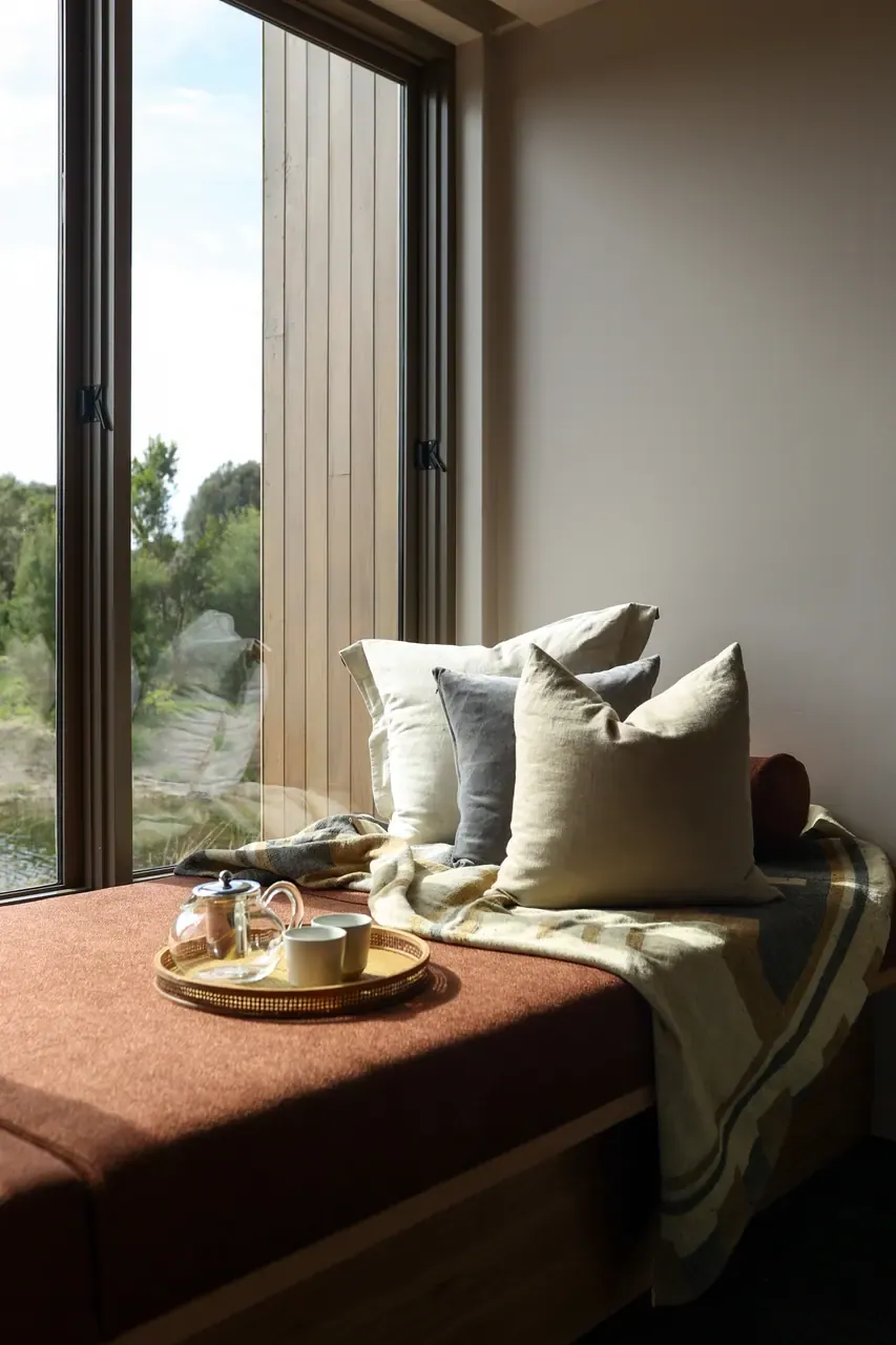 A tray with a glass teapot and two cups rests on a cushioned window seat in a Peninsula Hot Springs Eco Lodge room