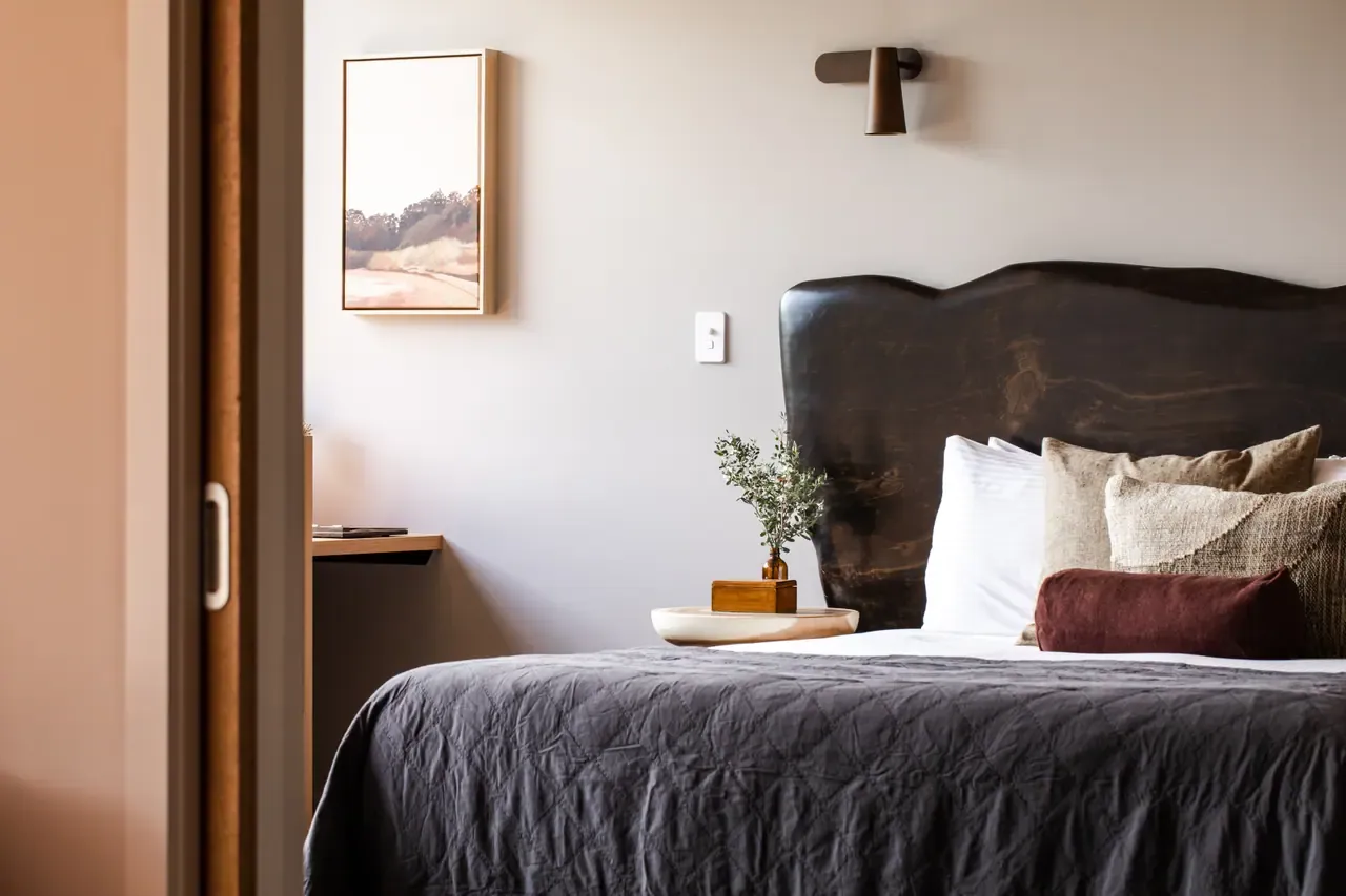 A bed with a dark timber headboard, linen cushions and grey quilt in an Eco Lodge room at Peninsula Hot Springs