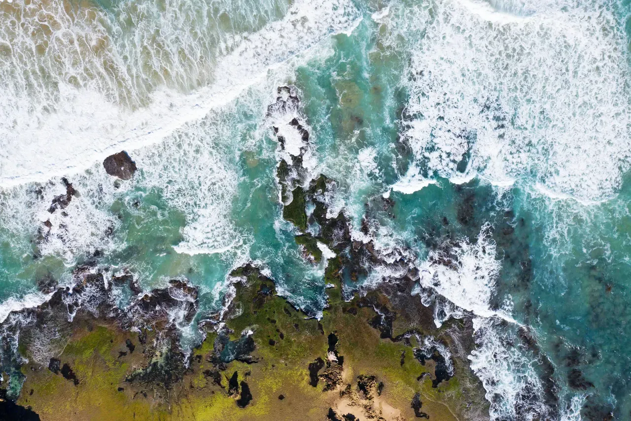 Overhead view of surf washing over dark rock shelves and green reef along the Sorrento Back Beach shoreline