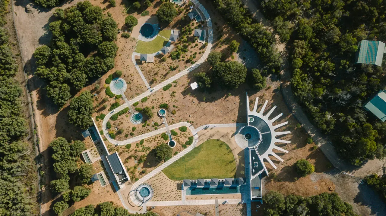 Aerial view of Alba Thermal Springs, with round pools linked by white paths, a lawn and a sunburst-shaped building amid bushland