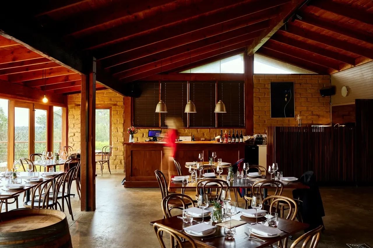 The timber-beamed dining room at Avani Winery, with bentwood chairs, set tables and a mudbrick wall behind the bar
