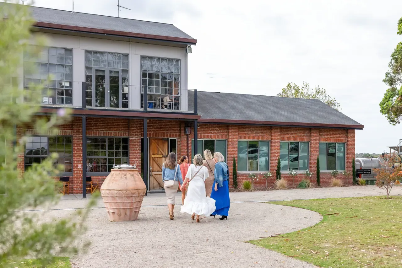 Group of women walking along a gravel drive towards the red-brick cellar door building at Trofeo Estate