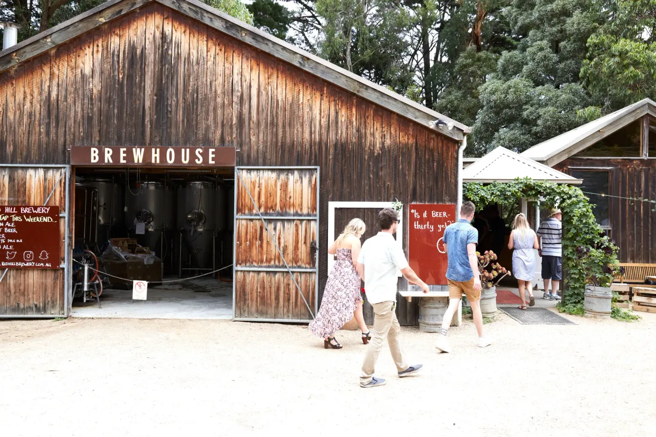 Visitors walk past the open doors of the weathered timber Brewhouse shed, with brewing tanks visible inside
